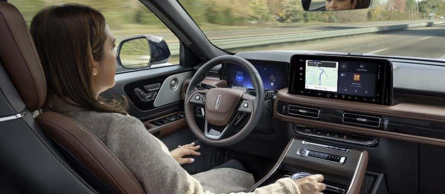 Woman driving a car with a modern interior, featuring a large touchscreen displaying navigation.