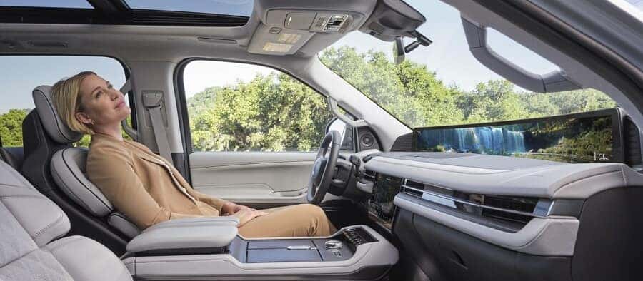 Woman relaxing in a luxurious car interior with a panoramic sunroof and scenic digital display.