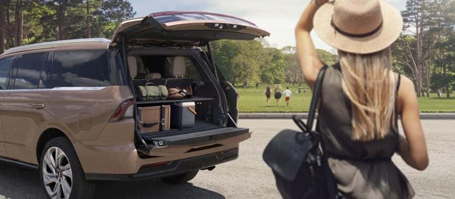 Woman with hat near SUV parked in a park, trunk open with camping gear visible.