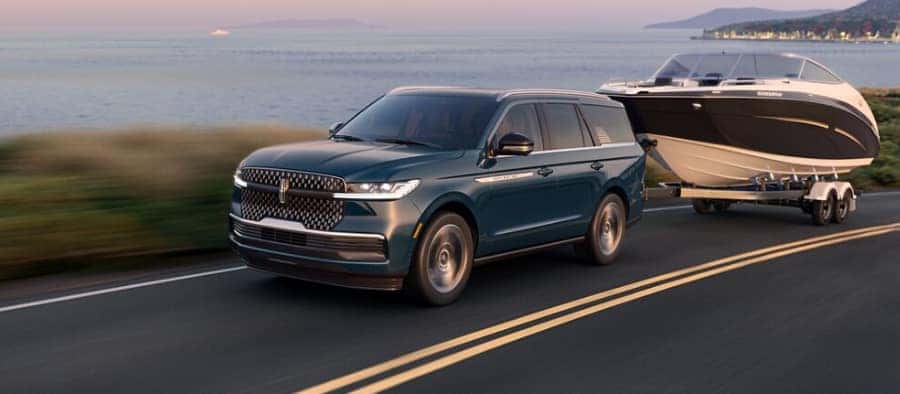 SUV towing a boat along a coastal road at sunset, featuring scenic ocean and landscape views.