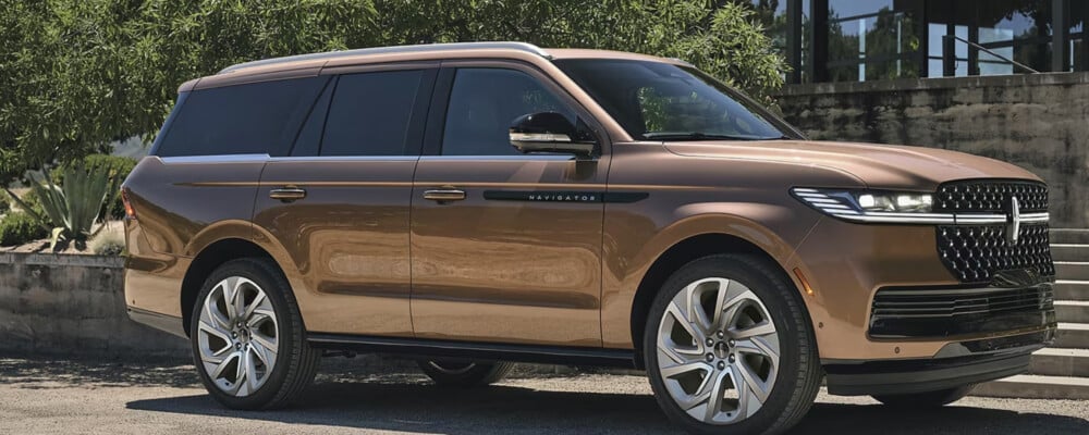 Bronze luxury SUV parked in front of lush greenery and a modern building.