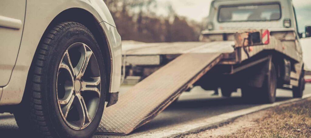 Car being loaded onto a tow truck on a roadside, wheel and ramp in focus.