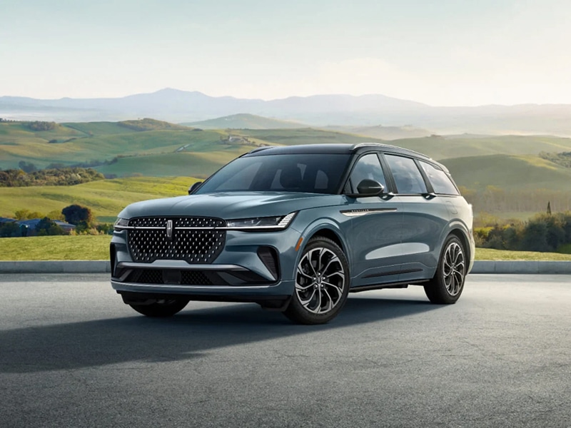 Sleek SUV parked on a road with lush green hills in the background under a clear sky.