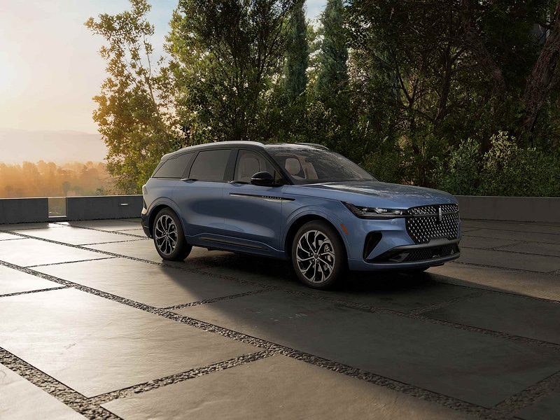Blue SUV parked on a stone driveway with trees in the background at sunset.