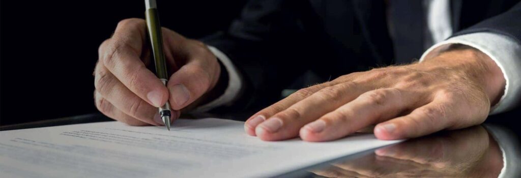 Close-up of a person signing a document on a reflective black surface, highlighting legal agreement.