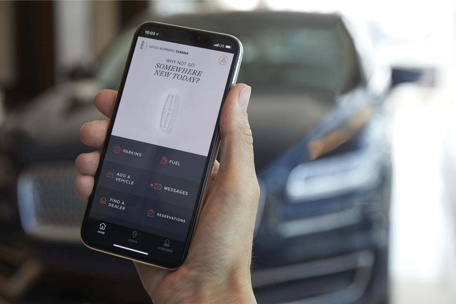 Person holding a smartphone displaying a car management app, with a blurred car in the background.