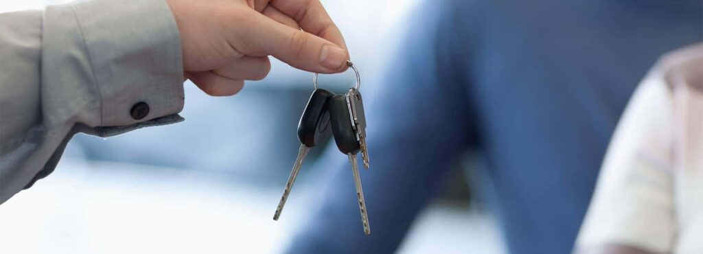 A hand passing over car keys, symbolizing a vehicle purchase or rental exchange.