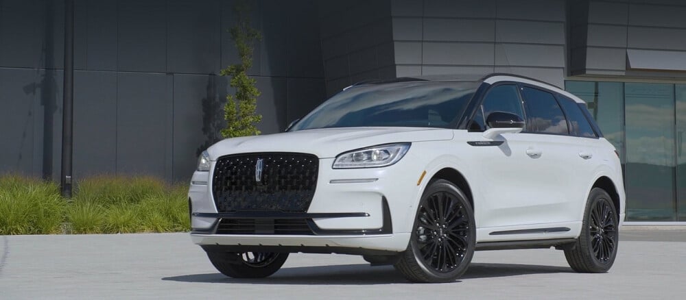 White SUV with black accents parked in front of a modern building, showcasing sleek design and style.