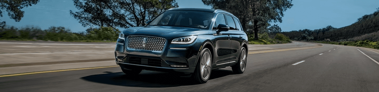 A sleek blue SUV drives on a scenic highway, surrounded by trees and a clear sky.