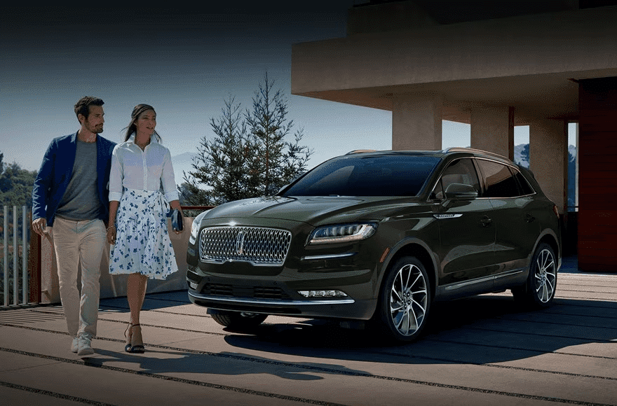 A man and woman walking beside a parked dark green SUV in a modern driveway setting.
